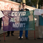 Covid Action activists stand with a banner reading COVID ACTION NOW in front of the memorial wall in central london.
