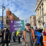 The Covid Action banner being held by a man in an FFP2 mask in the middle of a protest march to save the NHS.