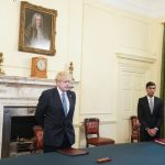 April 2020: The Prime Minister Boris Johnson in the Cabinet Room of No10 Downing Street, is joined by the Chancellor of the Exchequer Rishi Sunak (R) and they look small and impatient as there is a minutes silence for key workers claimed by the early pandemic.
