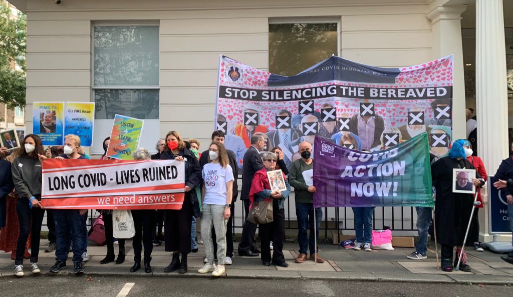 Protestors from assorted Covid activism groups (Long Covid Support, Covid Action, Bereaved Families) stand and hold banners outside the Covid-19 Public Inquiry.